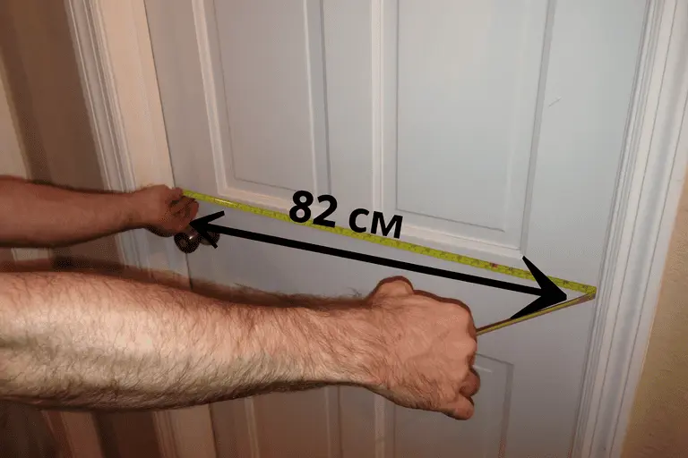Мастер в Москве измеряет рулеткой ширину дверного проёма — показано 82 см